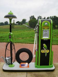 a green and black gas pump sitting on top of a cement slab next to a light pole