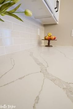 a kitchen counter with white marble and flowers in the vase on it's side