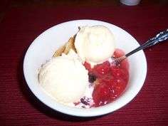 two scoops of ice cream sit in a white bowl with strawberries and bread