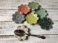 six ceramic flowers and a spoon on a wooden surface