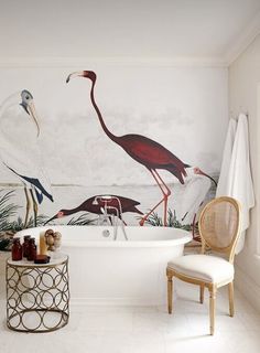 a bathtub with flamingos painted on the wall next to a chair and table