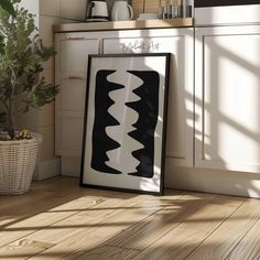 a black and white painting sitting on top of a wooden floor next to a potted plant