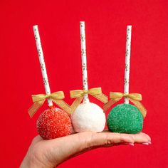 hand holding three christmas ornaments with candy on them and gold ribbon around the top, against a red background