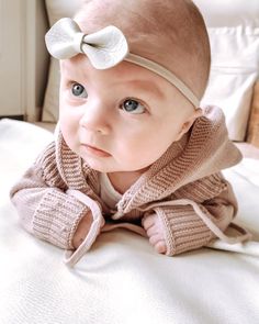 a baby with a white bow on her head laying on a bed looking at the camera