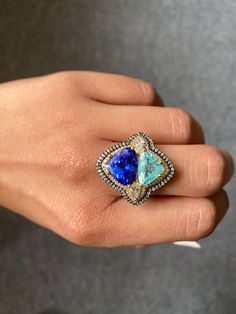 A unique cocktail ring with 5.17 carat natural Tanzanite and 2.66 carat natural Paraiba, with 0.61 carat 2 piece marquise shaped White Diamond and 0.79 carat round cut White Diamond, all set in solid 18K Gold. The rhodium polish in yellow and black, and the contrasting blue color of the trillion shaped gemstones make the cocktail ring a truly statement piece! The ring is currently sized at US 7, can be resized.  18K White Gold : 10.69 Grams  Tanzanite : 5.17 Ctw Paraiba : 2.66 Ctw Diamond : 1.4 Ctw Gia Certified Marquise Luxury Jewelry, Luxury Gia Certified Marquise Jewelry, Luxury Multi-stone Marquise Cut Rings, Luxury Marquise Cut Multi-stone Rings, Luxury Marquise Cut Sapphire Ring, Luxury Trillion-cut Sapphire Ring, Luxury Marquise Gemstone Ring, Luxury Marquise Cut Gemstone Ring, Luxury Marquise Cut Gemstone Jewelry