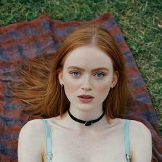 a woman with red hair is laying on a blanket and wearing a choker around her neck