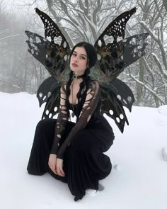 a woman sitting in the snow with a butterfly wings on her head and black dress