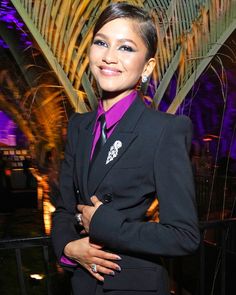 a woman in a black suit and purple shirt posing for the camera with her hands on her hips