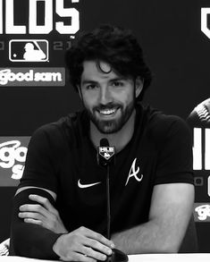 a man sitting at a table with a microphone in front of him and other baseball logos behind him