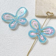 two blue and pink butterfly shaped hair pins on a white surface next to a piece of wood