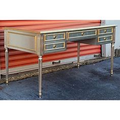 an antique desk with two drawers and gold trimmings on the top, sitting in front of a red wall