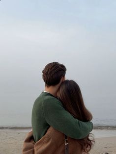 a man and woman hug on the beach while looking at an airplane in the sky