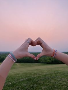 two hands making a heart shape with their fingers in front of a field at sunset