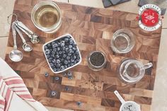 a cutting board topped with bowls and measuring spoons next to cups filled with blueberries