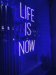 a neon sign that says life is now on the side of a building in front of a window