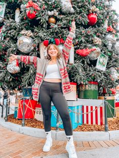 a woman standing in front of a christmas tree wearing leggings and a sweater