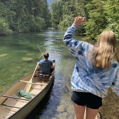 a man and woman in a canoe on the river with their hands up to the sky