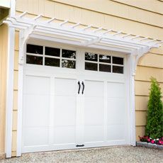 two white garage doors with windows on the side of a house in front of a planter