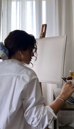 a woman in white shirt painting on easel