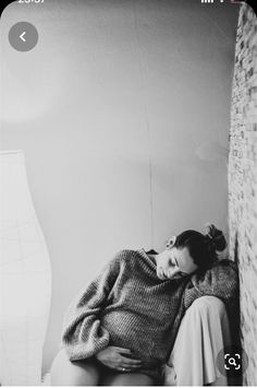 a woman sitting on top of a bed next to a brick wall with her head down