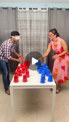 a man and woman standing next to a table with plastic cups on top of it