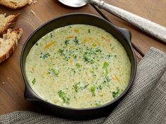 a bowl of broccoli cheese soup on a table with bread and spoons