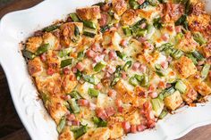 a casserole dish with ham, green onions and cheese on it sitting on a wooden table