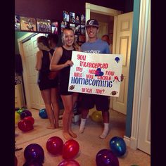 two people holding up a sign in front of balloons and confetti on the floor