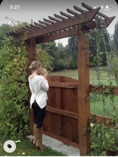 a woman standing in front of a wooden structure with vines growing on the top and bottom