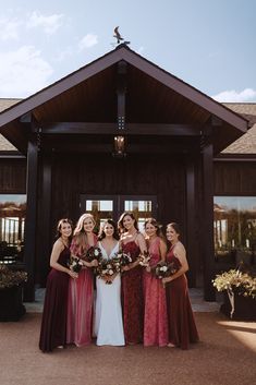 a group of women standing next to each other in front of a wooden building holding bouquets