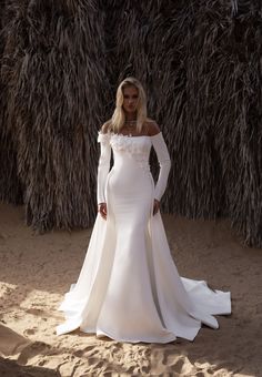 a woman in a white wedding dress standing on the beach with her arms behind her back