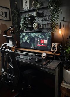 a desk with a computer monitor, keyboard and speakers on it next to potted plants