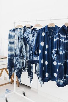 three shirts hanging on a clothes rack in front of a white wall and wooden table