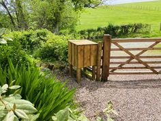 a wooden gate in the middle of a gravel area next to green grass and trees