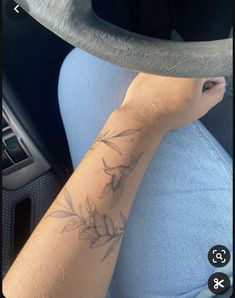 a person with a tattoo on their arm sitting in a car and holding the steering wheel