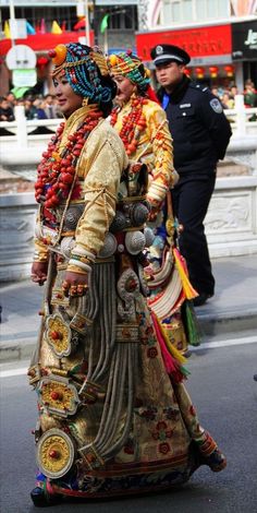 two people dressed in elaborate clothing walking down the street with police officers standing behind them