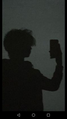 the shadow of a person holding a cell phone in their hand, against a dark background