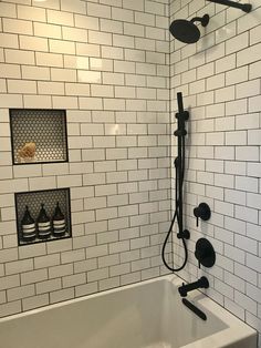 a bathtub with black fixtures and white tiles on the walls, in a bathroom