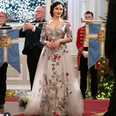 a woman in a long dress walking down the aisle with other people watching from behind her