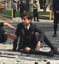 two boys in uniforms sitting on the ground with their hands together and pointing at them