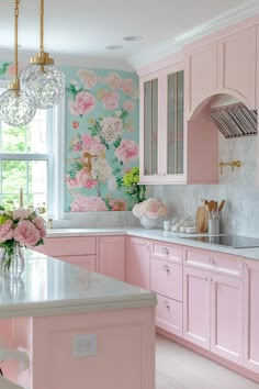 a kitchen with pink cabinets and marble counter tops, an island in the middle has flowers on it