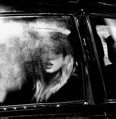 a black and white photo of a woman sitting in a car looking out the window