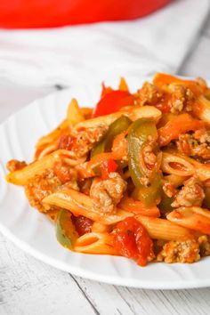 a white plate topped with pasta and meat covered in sauce on top of a wooden table