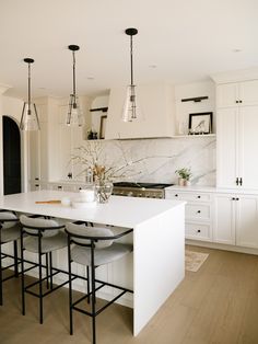 a kitchen with white cabinets and stools next to a center island in front of an oven