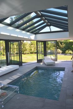 an indoor swimming pool surrounded by glass walls and windows with sun shining through the roof