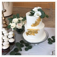 a white and gold wedding cake sitting on top of a table next to cupcakes