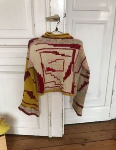 a knitted sweater hanging on a hook in front of a white door with wood flooring