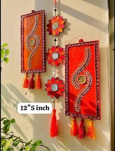 two red and orange wall hangings with tassels attached to the side of a building