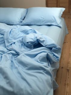 an unmade bed with light blue sheets and pillow cases on top of the bed