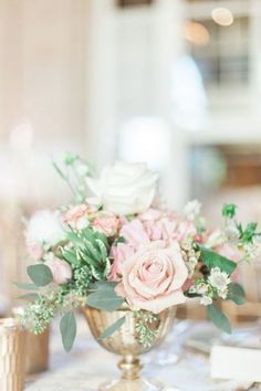 a vase filled with pink and white flowers on top of a table next to gold cups